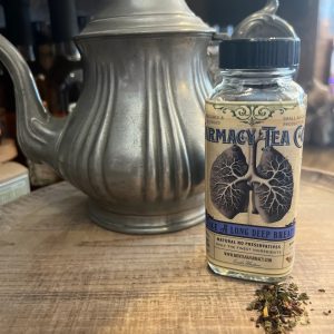 Glass jar of Take a Long Deep Breath Respiratory Support Herbal Tea by Farmacy Tea Co., with loose herbs beside it and a vintage teapot in the background
